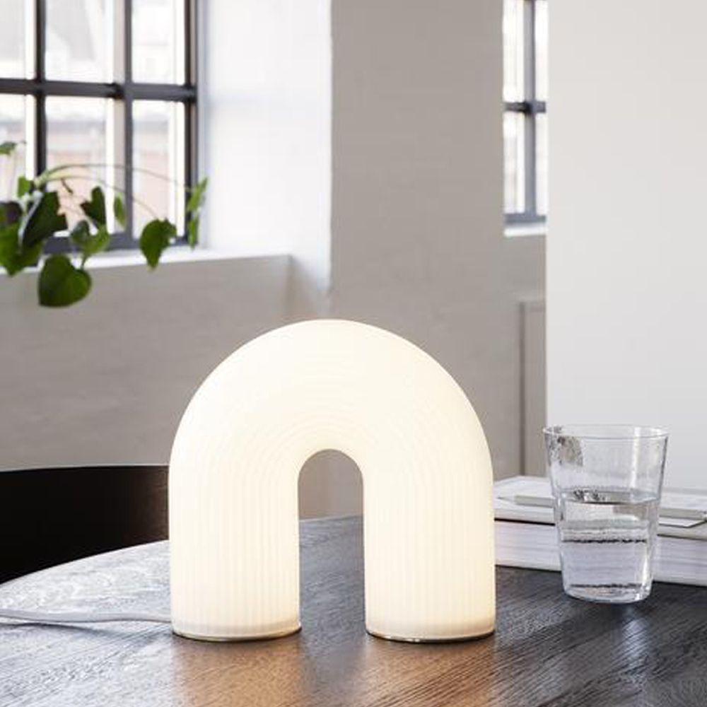 Die bogenförmige Ferm Living Tischleuchte spendet nicht nur Licht, sie ist auch einfach ein wunderschönes Design-Objekt. 