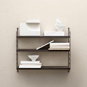 Minimalismus im Winter: Herrlich entschleunigend! 3 Das dunkle String Furniture Pocket Regal an einer hellen Wand mit Büchern und ausgewählten Objekten.