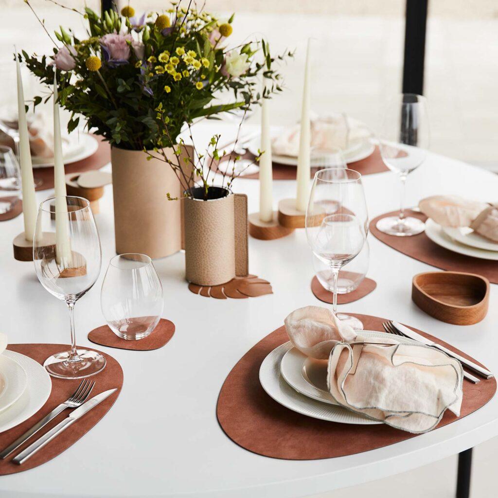 Moderne Osterdeko ohne Kitsch und Gelb: Stilvolle Ideen für Ihren Ostertisch 1 Gedeckter Tisch mit Tischsets aus Leder in Braun, Kerzen und zwei unterschiedlich großen Blumenvasen. Denn moderne Osterdeko ist minimalistisch.